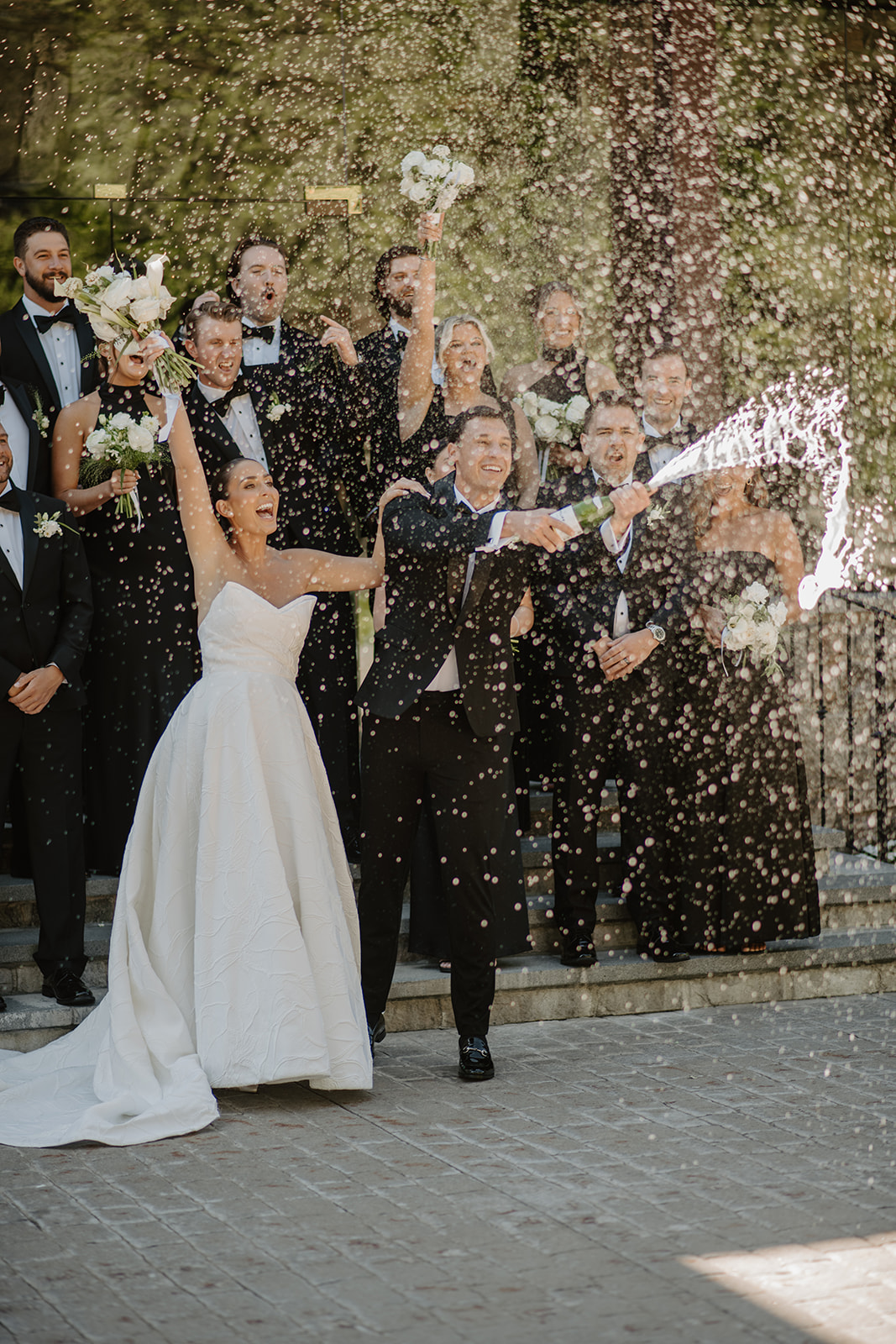 Groom spraying champagne in front of a cheering bride and wedding party on the steps of Le Chateau.